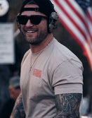 Man wearing Savage Tacticians t-shirt, sunglasses, and headset outdoors with American flag