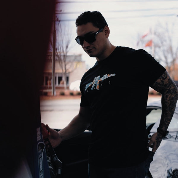 Man wearing Savage Tacticians graphic t-shirt and sunglasses pumping gas outdoors