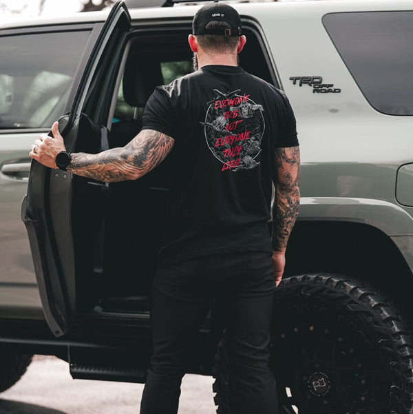 Savage Tacticians tattooed man wearing black graphic t-shirt next to TRD Off Road SUV